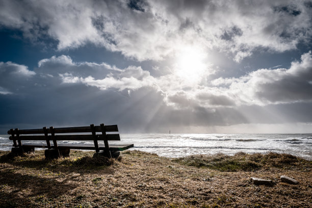 法国雷岛里韦杜海滩上的木制长凳。太阳在乌云中闪耀。图片下载