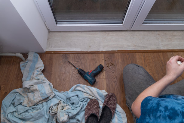 钻头在地板上。建造者铺好层压板，并在层压板和瓷砖之间放一个角。图片下载