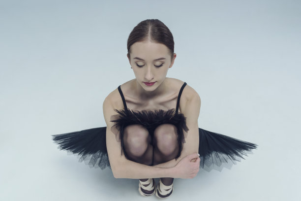 一个芭蕾舞女演员的肖像在黑色芭蕾舞裙蹲抱她的膝盖图片下载