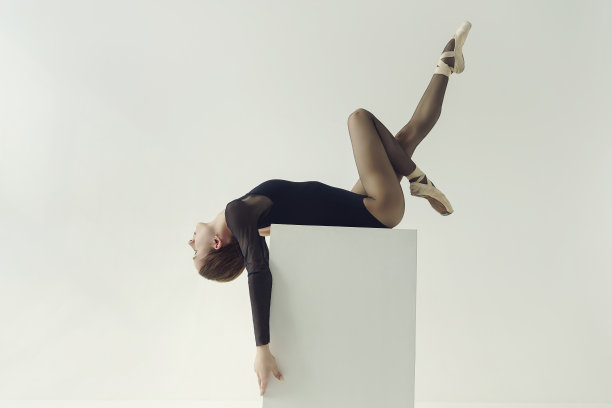 一个穿着黑色紧身衣的芭蕾舞演员躺在一个立方体上，头向后仰，一条腿向上伸展图片下载