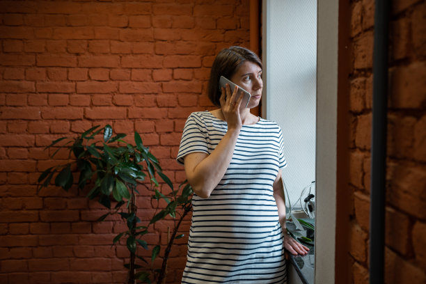 孕妇在办公室靠窗用智能手机通话。图片下载