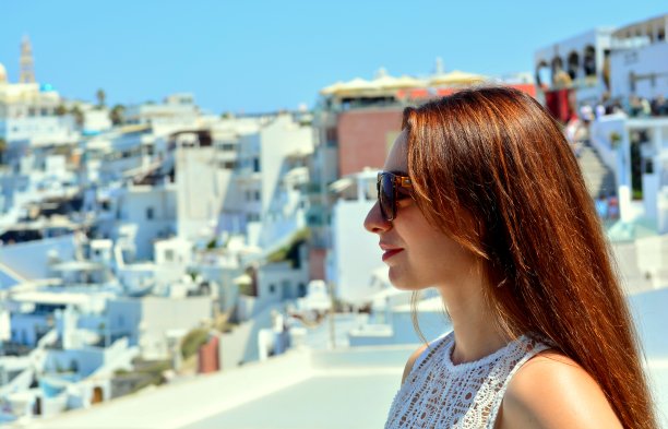 年轻的黑发女子戴太阳镜的肖像，侧面视图，与Fira镇在夏天的背景，圣托里尼岛，希腊，欧洲1图片下载