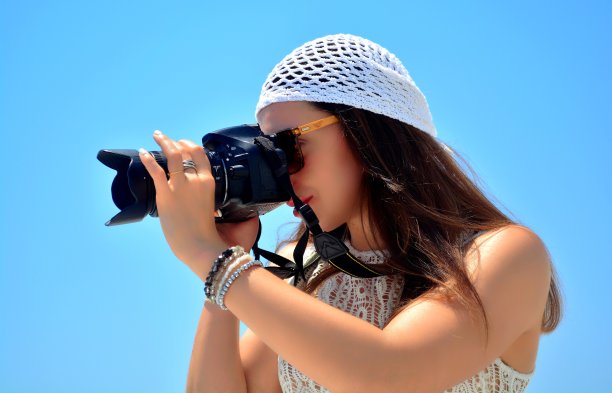 年轻的黑发女摄影师的肖像戴白色波西米亚钩针帽子对蓝天，费拉，圣托里尼岛，希腊，欧洲图片下载
