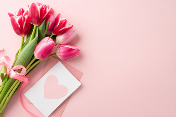 母亲节的概念。顶部视图照片的粉红色郁金香束系与丝带和信封与明信片在孤立的粉彩粉红色背景与复印空间图片下载