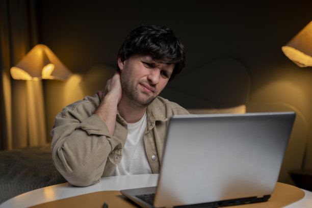 年轻沮丧的自由职业者正在经历严重的颈部疼痛。他在他的家庭办公室里，坐在他的现代工作场所，痛苦地按摩着它图片下载