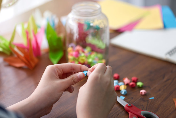 女人的手从彩色折纸折叠一颗星星作为礼物或装饰的节日的幸福和希望。图片下载