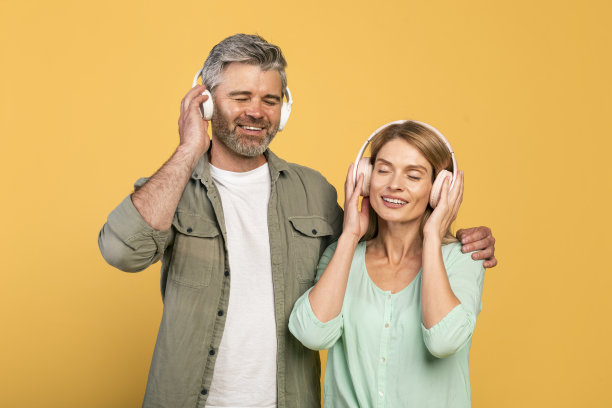 戴着耳机，闭着眼睛听音乐，黄色背景的中年白人夫妇图片下载