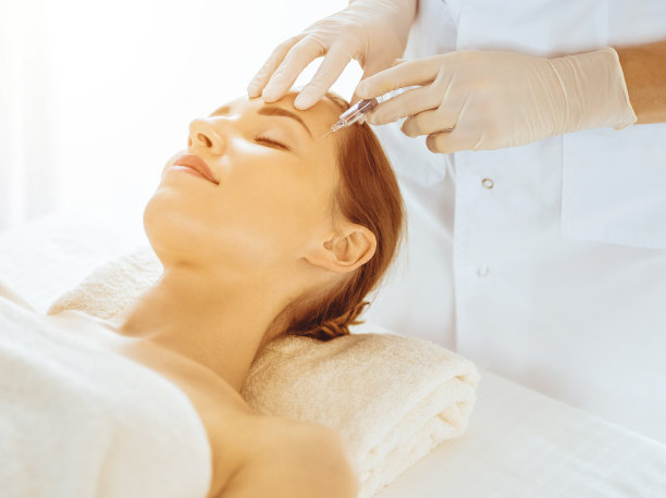 美女在阳光明媚的医疗中心闭着眼睛接受美容注射。美容师医生用注射器给女性面部做美容手术图片下载