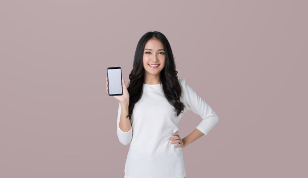 美丽的亚洲女子在孤立的棕色背景上持有空白屏幕的智能手机模型图片下载