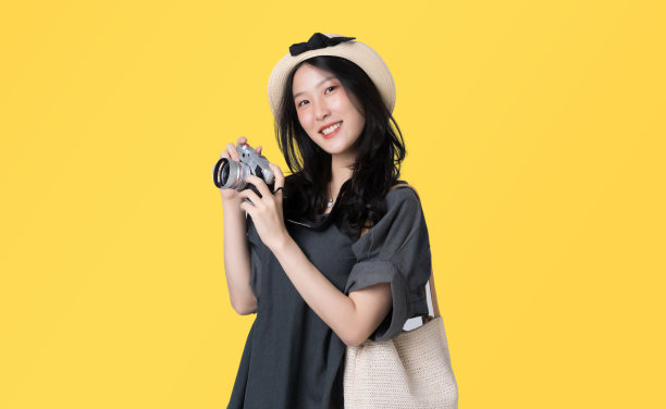 年轻的亚洲女子穿着带有遮阳帽和太阳镜的连衣裙，拿着相机在黄色背景下隔离旅行概念。图片下载