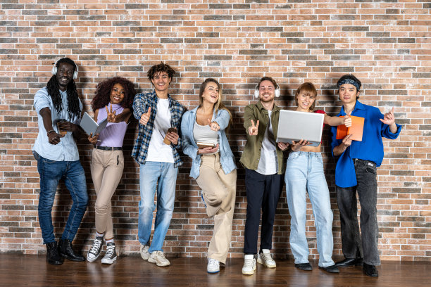 年轻的学生以积极微笑的态度，一群朋友在砖墙前摆姿势，快乐微笑的表情捧着书、日记、笔记本电脑图片下载