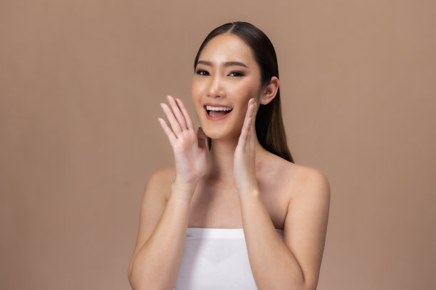 美丽的亚洲女性触摸眉毛微笑，皮肤干净清新，快乐与积极的情绪，隔离在米色背景上，美容化妆品和水疗面部护理概念。图片下载