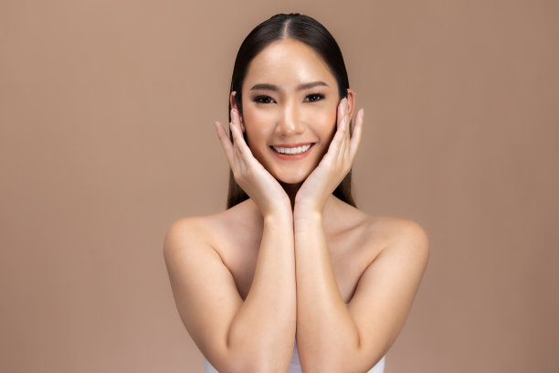 美丽的亚洲女性触摸眉毛微笑，皮肤干净清新，快乐与积极的情绪，隔离在米色背景上，美容化妆品和水疗面部护理概念。图片下载