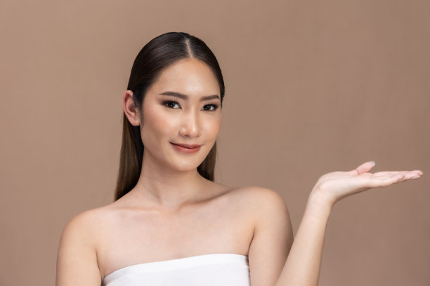 美丽的亚洲女性触摸眉毛微笑，皮肤干净清新，快乐与积极的情绪，隔离在米色背景上，美容化妆品和水疗面部护理概念。图片下载