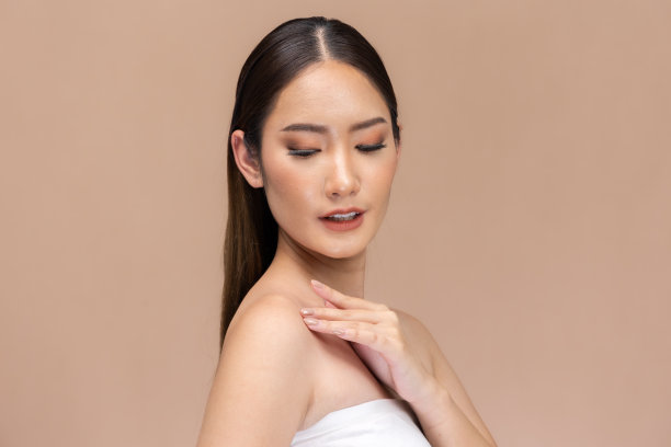 美丽的亚洲女性触摸眉毛微笑，皮肤干净清新，快乐与积极的情绪，隔离在米色背景上，美容化妆品和水疗面部护理概念。图片下载