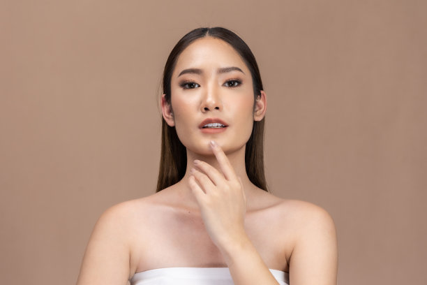 美丽的亚洲女性触摸眉毛微笑，皮肤干净清新，快乐与积极的情绪，隔离在米色背景上，美容化妆品和水疗面部护理概念。图片下载