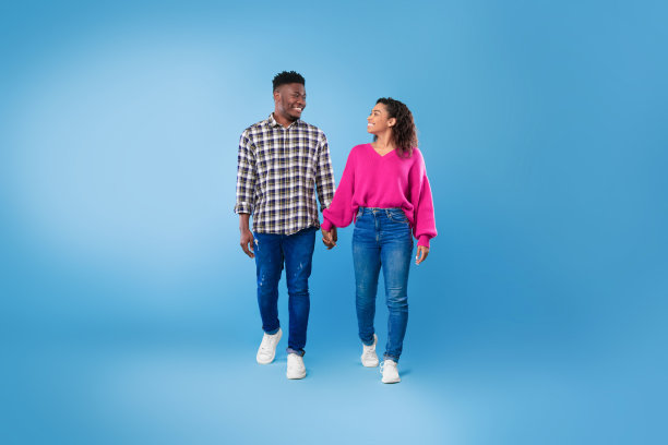 快乐的千禧一代黑人夫妇走着，手牵着手，看着对方在蓝色的演播室背景，全长图片下载
