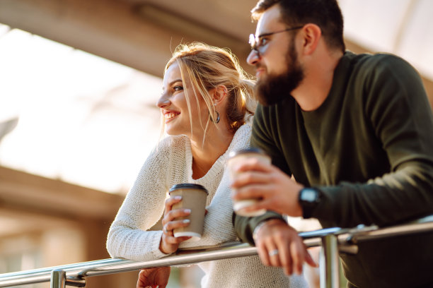 年轻的夫妇聊天，喝着咖啡，走在早晨的城市。图片下载