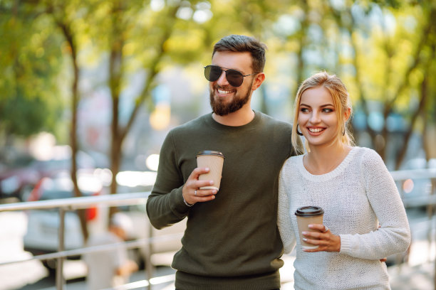 年轻的夫妇聊天，喝着咖啡，走在早晨的城市。图片下载