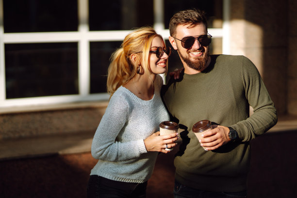 年轻的夫妇聊天，喝着咖啡，走在早晨的城市。图片下载