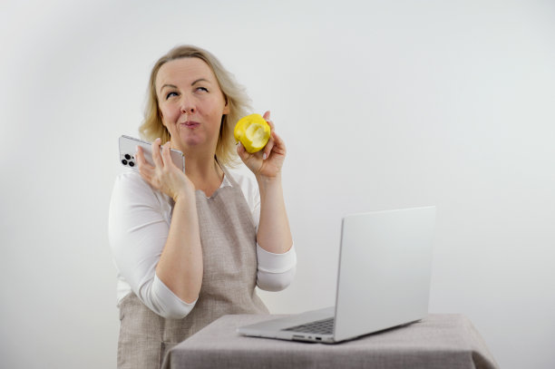 有见识的女人很高兴举起手指，家庭主妇手里拿着手机笔记本电脑吃苹果，抬起眼睛望着天花板，压着嘴唇，吃饱了嘴，厨房围裙做饭这就是我今天要做的东西图片下载