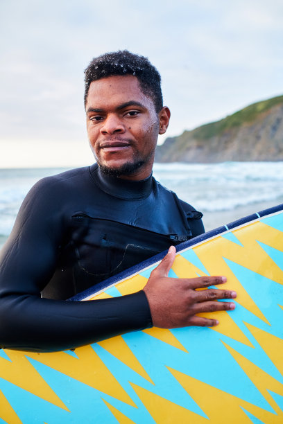 一个年轻的非洲裔美国人的肖像，他的冲浪板与大海的背景图片下载
