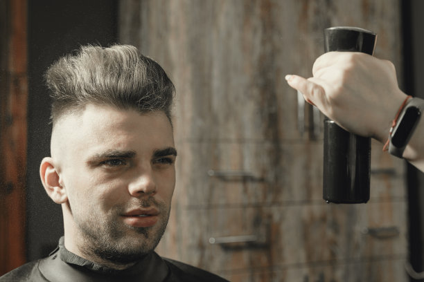 美发师女孩喷发胶年轻男子坐在椅子上在理发店图片下载