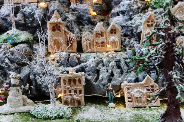 风景圣诞村展示的全帧图像，人造塑料和木制圣诞树在人造草和雪上，周围是发光的自制木屋和雪人，重点在前景图片下载