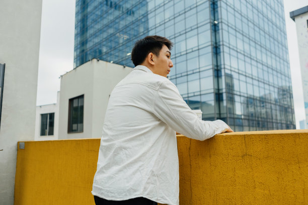 在一个阴天，一个男性商人的剪影出现在公司外的阳台上，喝着咖啡——平衡工作和生活图片下载