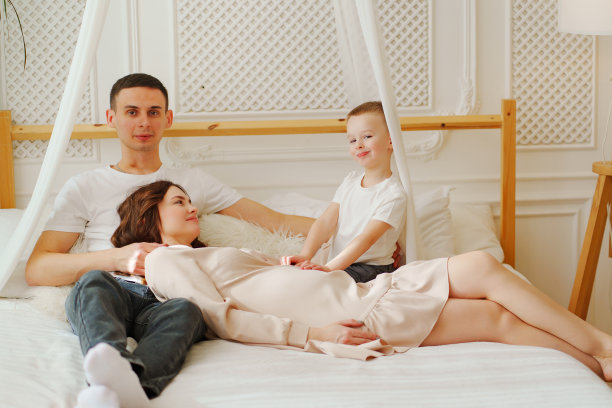 快乐的怀孕妈妈，爸爸和儿子在床上玩耍。家庭幸福的观念。图片下载
