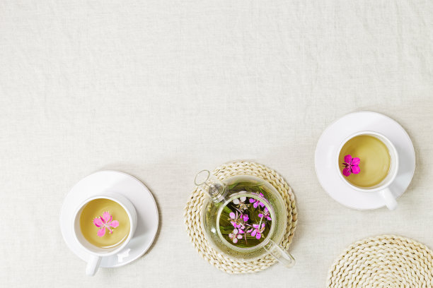 白色茶杯和透明玻璃茶壶中的杂草茶，用伊凡柴的绿叶制成的草药热茶，铺在纺织桌布上。俯视图健康饮品和野生开花杨柳，茶点时间图片下载