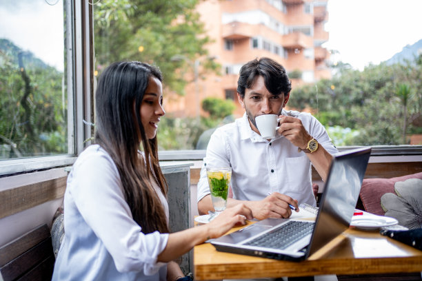 一个成熟的男人在咖啡店喝咖啡，而他的同事在用笔记本电脑图片下载