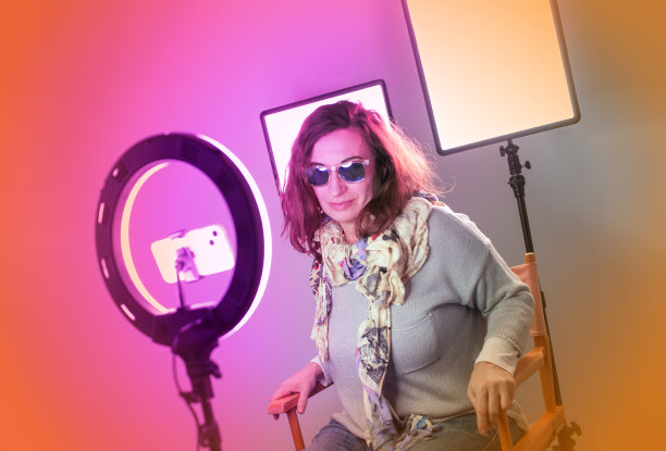 快乐的女网红坐在戒指灯旁使用智能手机图片下载