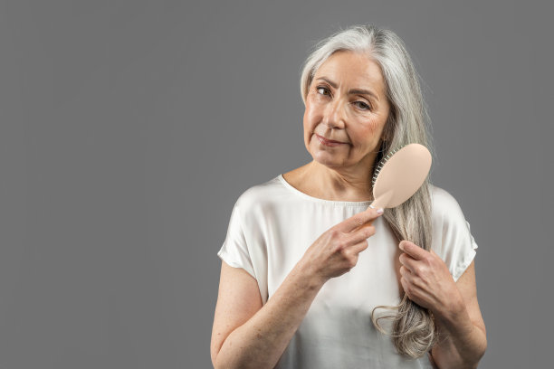 严肃的资深白人女性用梳子梳理她的灰色头发，孤立在灰色背景，工作室图片下载