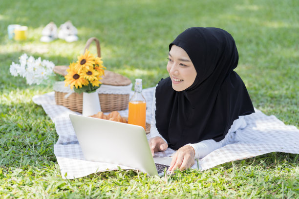 亚洲年轻的穆斯林妇女戴着头巾使用笔记本电脑与快乐和微笑在公园野餐假日周末图片下载