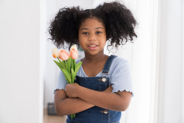 非裔美国女孩站在那里，手里拿着郁金香花，开心地笑着。头发卷曲的黑孩子女孩在家放松地站着图片下载