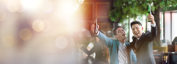 两个西装革履的亚洲商务男士在办公空间拿着瓶子一起举手，心情愉快，面带微笑，完成了完成的工作和团队合作成功的理念图片下载