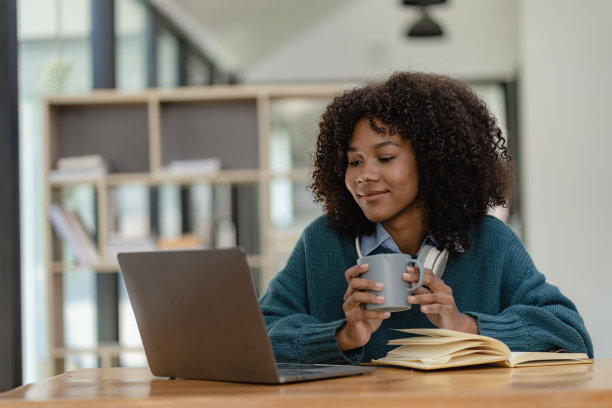 年轻女学生戴着耳机学习在线培训视频交流快乐的女学生看着电脑屏幕，观看网络研讨会或在图书馆的网络摄像头视频聊天。图片下载