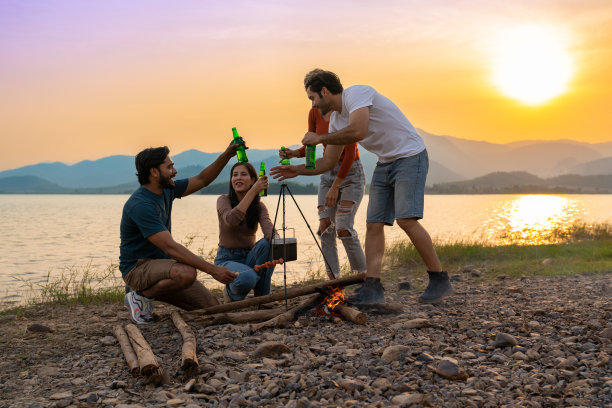 一群快乐的多种族朋友在日落时分在湖边举行了篝火晚会图片下载