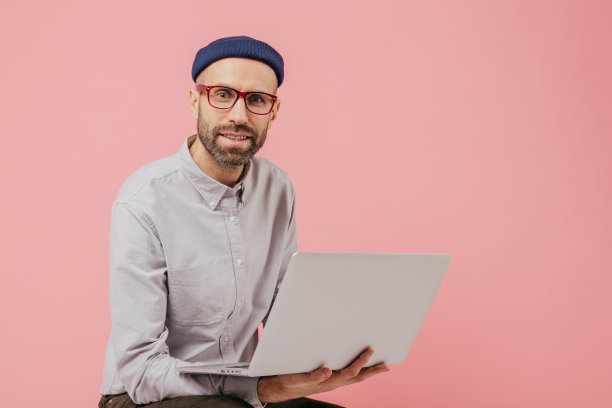 不刮胡子的男博主更新个人资料，浏览社交网络，与粉丝分享多媒体文件，连接无线网络，手持笔记本电脑，穿着时髦的正装图片下载