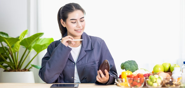快乐的女性专业营养健康的包围着各种新鲜水果和蔬菜工作的数字平板电脑和微笑。正确的营养饮食观念，保健饮食。图片下载