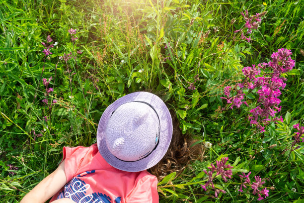 一个孩子的肖像戴着帽子，他的脸在夏天躺在草地和野花。帽子上有猫一样的眼睛和耳朵，夏天的时候，自由自在图片下载