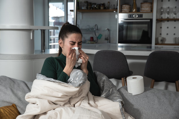 生病心烦意乱的年轻女子坐在沙发上盖着毯子冻着擤鼻涕发烧感冒打喷嚏在纸巾，生病的女孩有流感症状在家咳嗽，流感概念图片下载