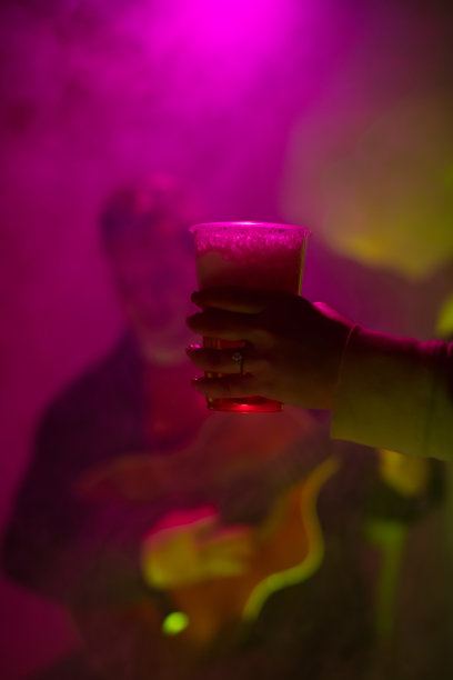 一名女子拿着一个塑料啤酒杯，在俱乐部背景中有一位音乐家在弹吉他。图片下载