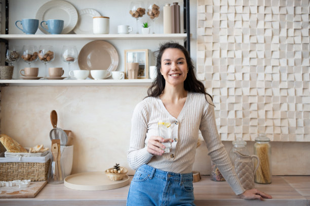 健康水合概念。快乐的年轻女士，站在家里的现代厨房内部喝水图片下载