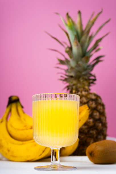 一杯菠萝汁的侧视图和亮粉色背景上的菠萝图片下载