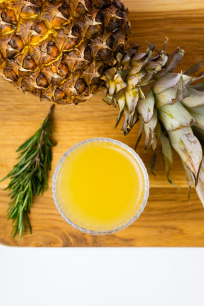 一杯菠萝汁和一个放在木托盘上的菠萝图片下载