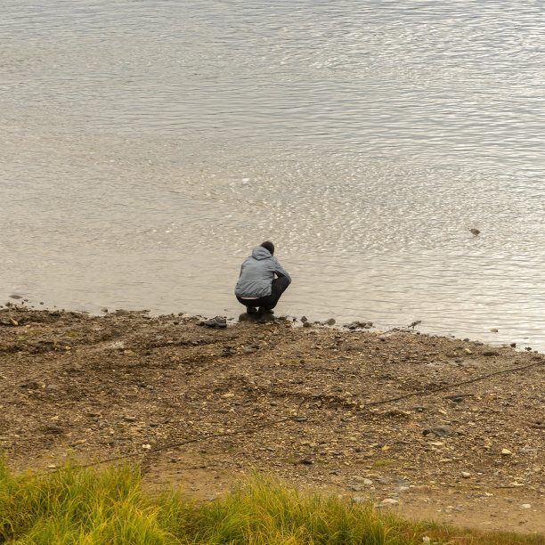 清晨，一名游客坐在河边，洗着沾满泥土的运动鞋图片下载