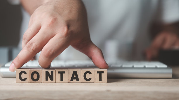男子用手把带有CONTACT文字的木块立方体放在键盘前。客户支持概念。图片下载