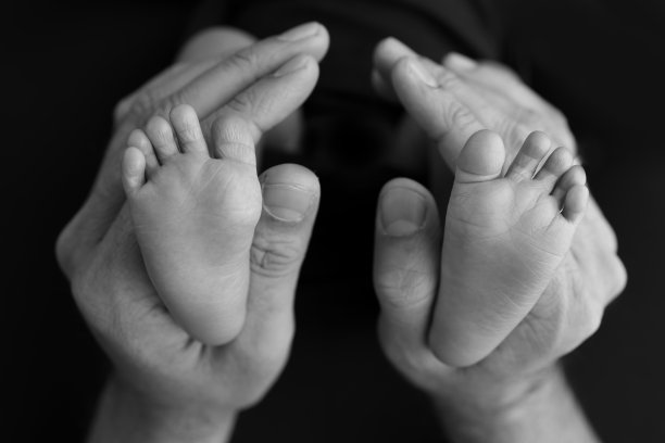 黑色和白色的阴影美丽的形状的母亲的手，抱着小新生儿的脚在黑色的背景与爱，关心，家庭安全和保护，早产的概念或新生儿监护图片下载